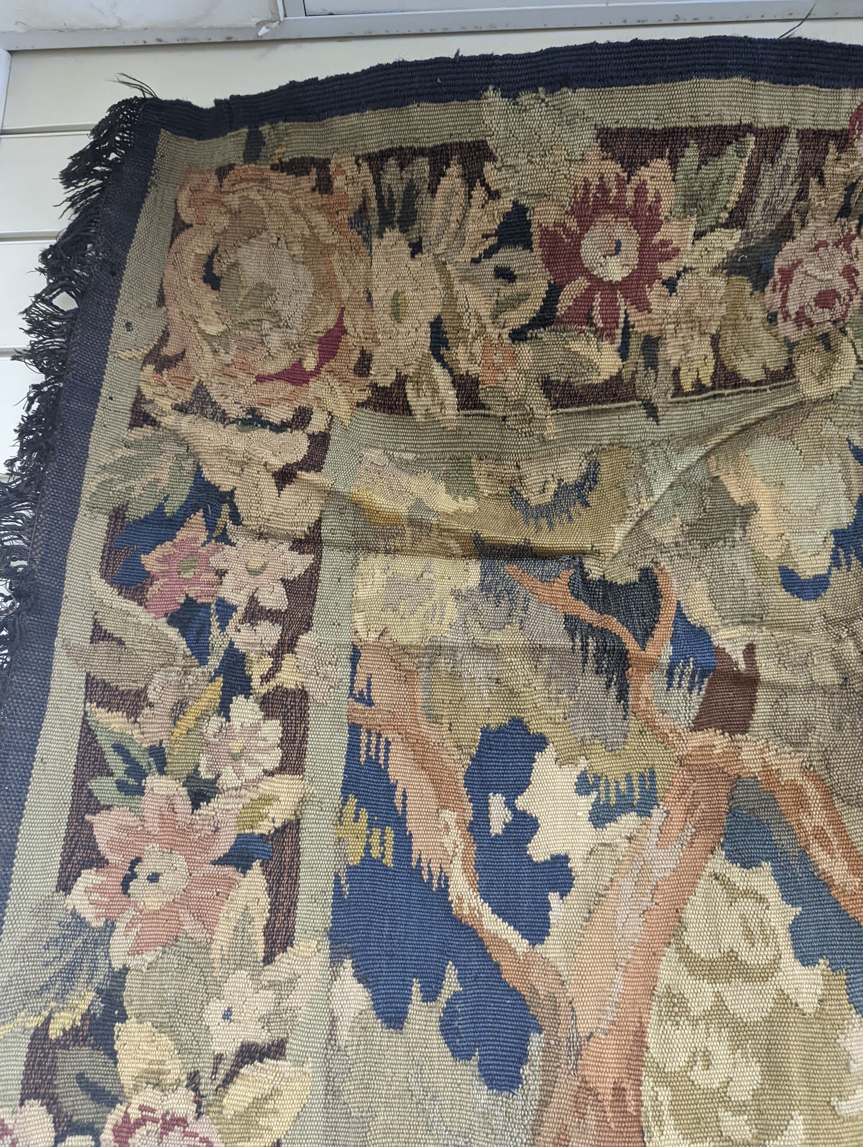 A late 19th / early 20th century French tapestry depicting a woodland scene with trees and flowers with a floral border woven in autumnal colours
